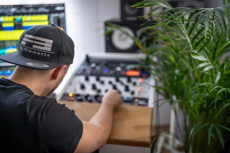 Mann mit Mütze bedient ein Synthesizer-Equipment neben einer Pflanze.