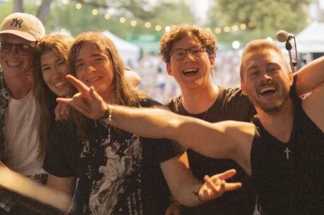 Gruppe junger Leute posiert fröhlich vor einer Menge bei einem Musikfestival.